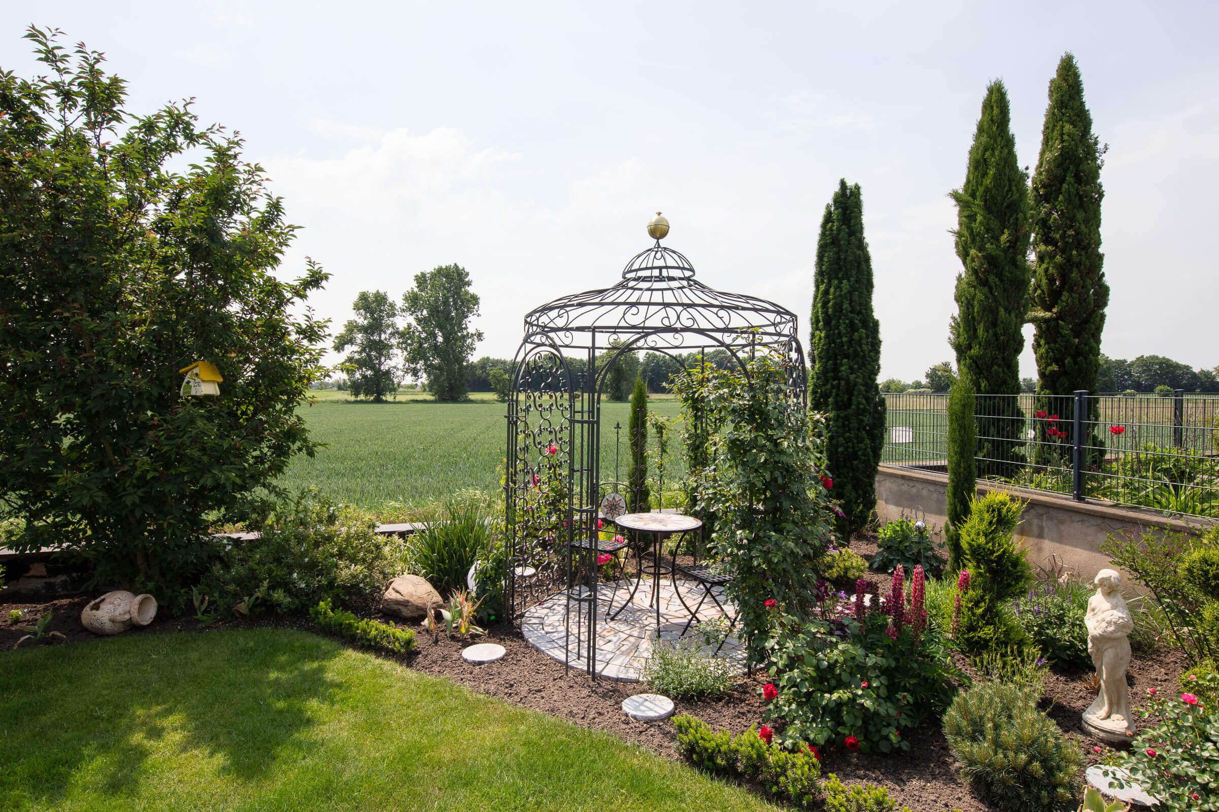Gartenpavillon Siena eingerichtet und mit Rosen berankt in einem Garten