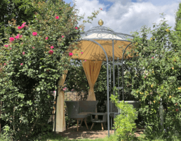 Pavillon Milano in pulverbeschichteter Ausfuehrung mit Sonnensegel und Vorhaengen in einem gruenen Garten